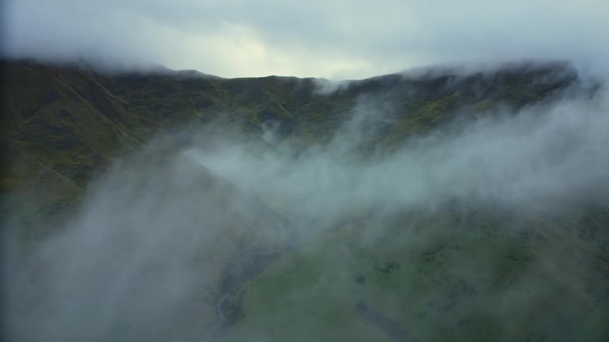 A verdant mountain ridge obscured by clouds during the day