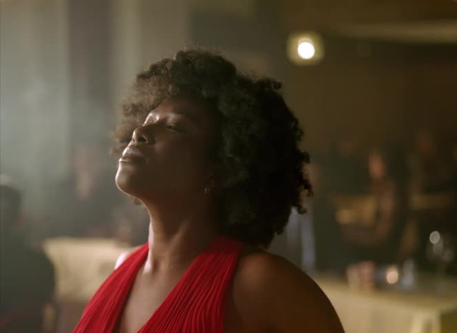 People watch female dancer with curly hair earrings and red dress starting to dancing in bar