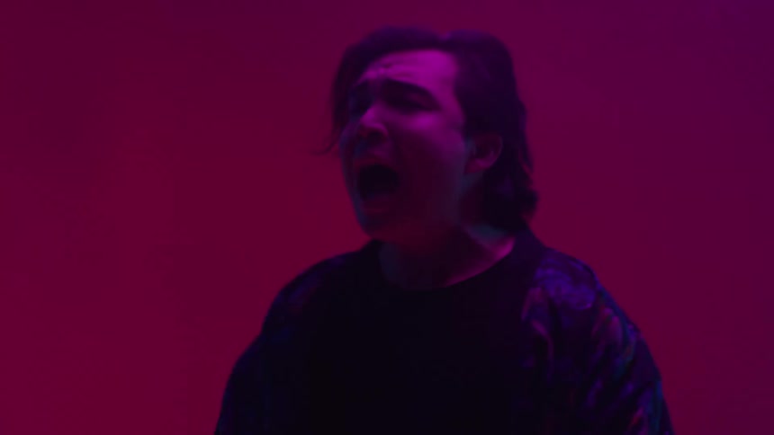 The lead singer dances and sings as the band plays and colorful lights glow
