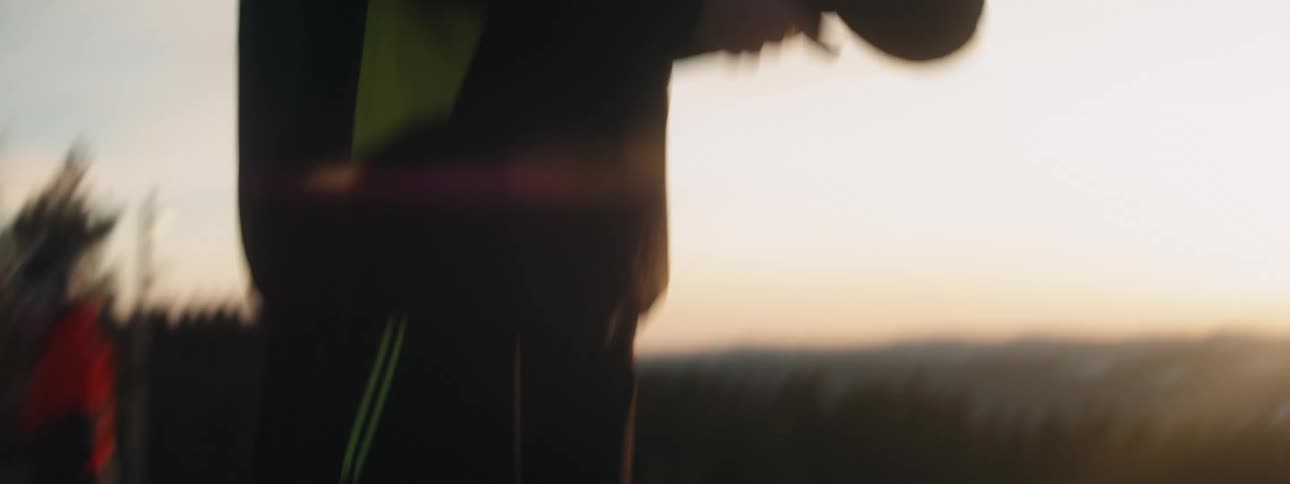 A snowboarder adjusts their helmet and puts on gloves while standing on a mountain slope in the evening