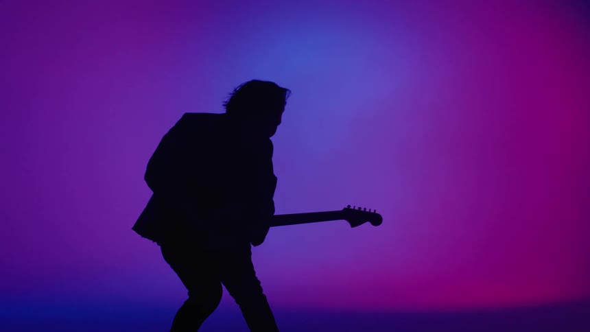 A man is on a stage with multi color lights playing guitar