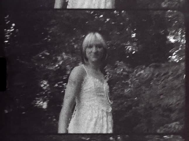 A barefoot woman is standing outside near trees twirling around and showing off her white dress