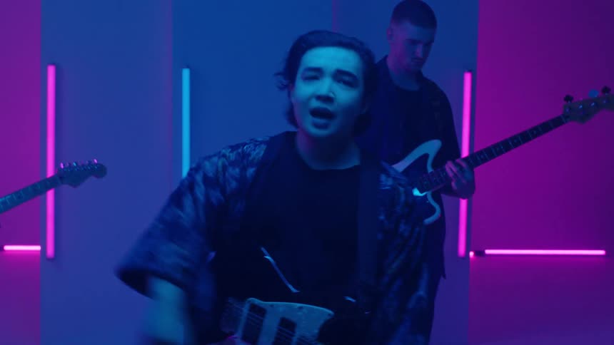 Rock band frontman sings to the camera with his group on a colorful stage