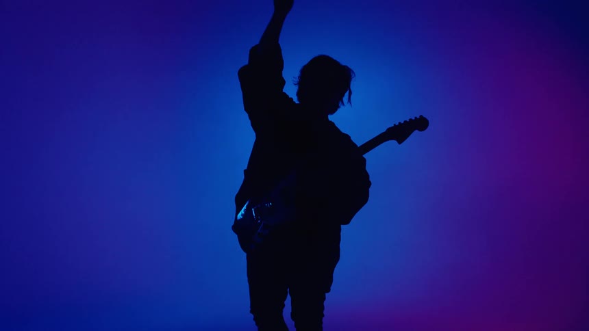 Guitarist plays instrument while silhouetted against colorful background
