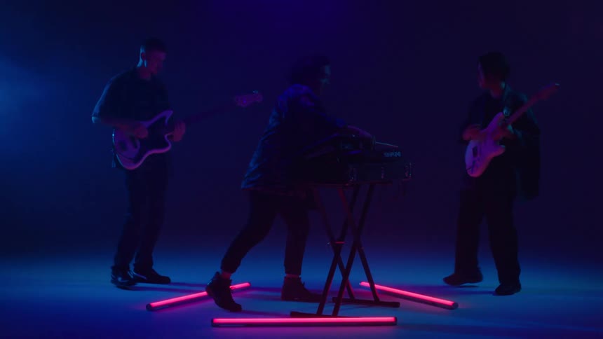 Band of happy excited musicians playing on stage under colorful changing lights
