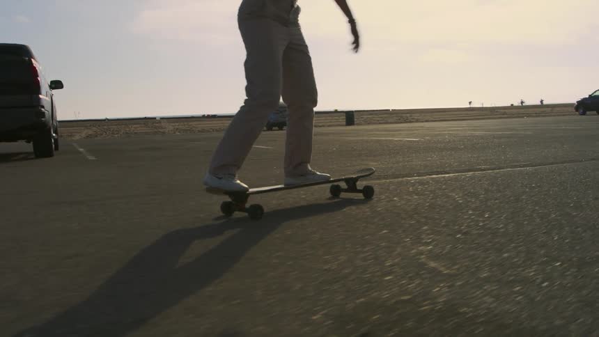 A teenager rides a skateboard through a parking lot