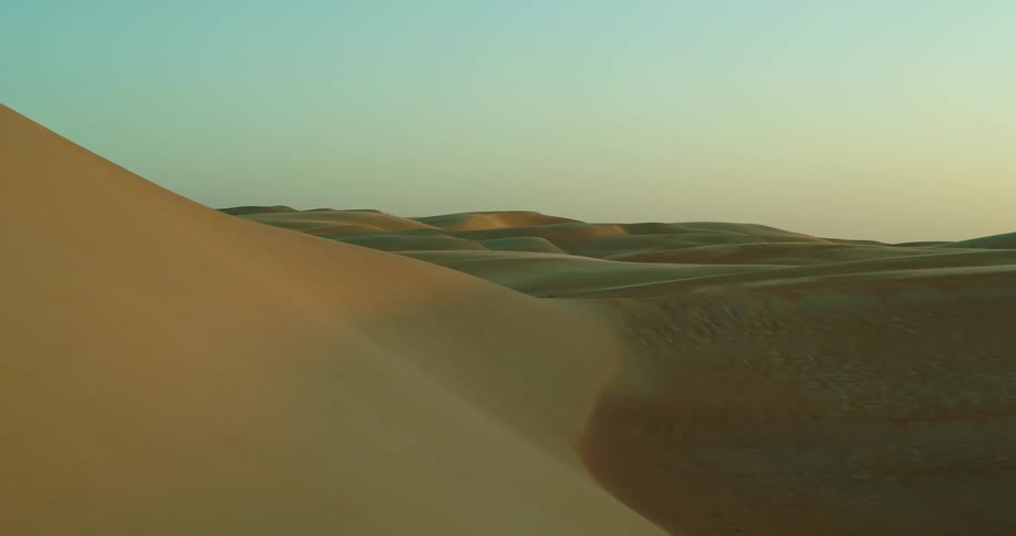 An aerial view of sand dunes in a desert at sunrise