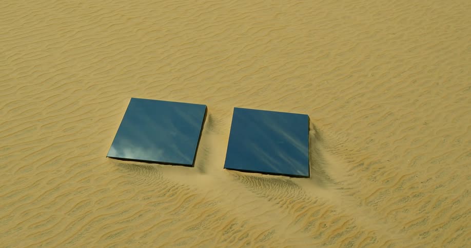 A pair of large mirror panels lying in the sand of a desert during the day