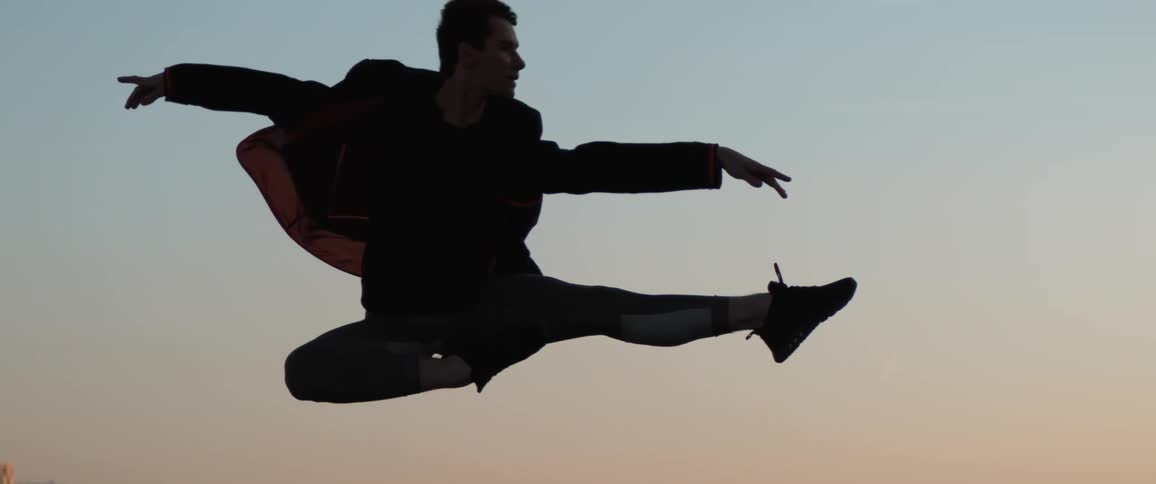 The silhouette of a male dancer leaping into the air with arms and legs extended