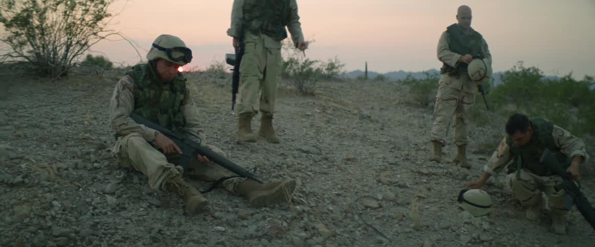 Military personnel carrying weapons sitting and standing on the slope of a ridge getting some rest