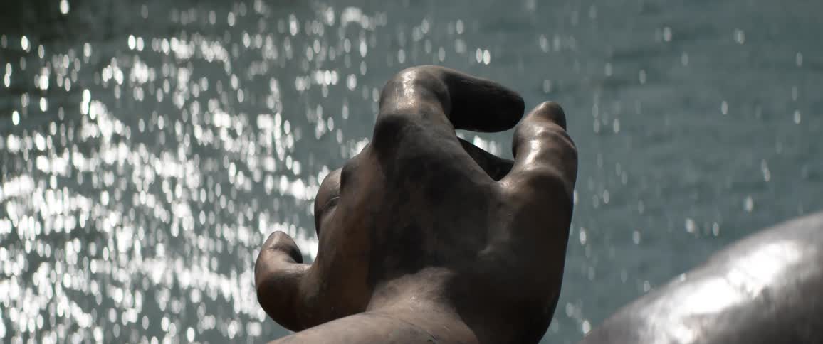 A statue of a persons hand is over the water
