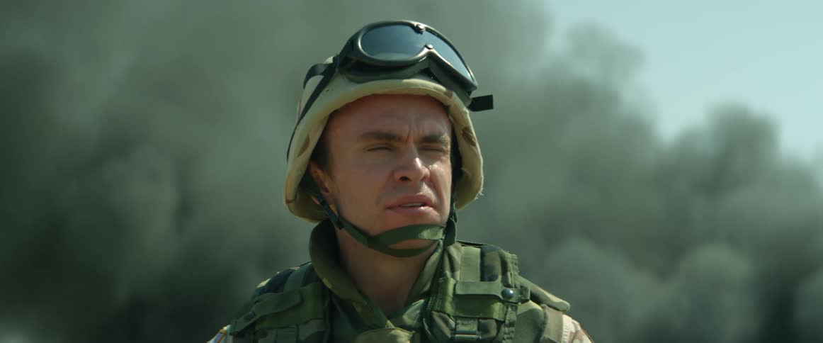 Close up of the face of a soldier wearing a helmet in front of rising clouds of smoke
