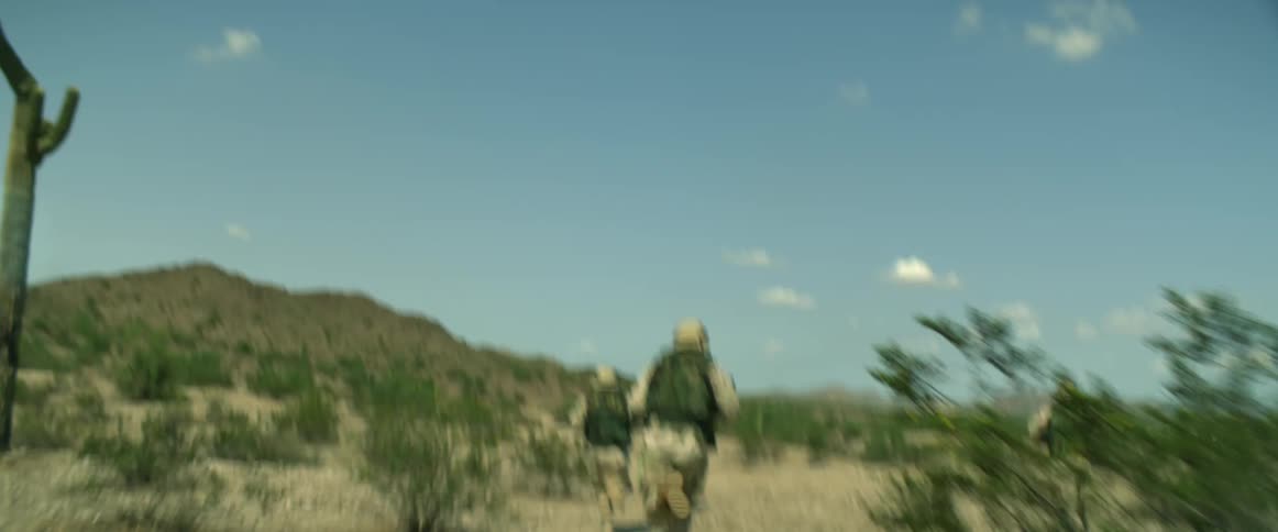 Soldiers run across desert scrub toward hills on horizon