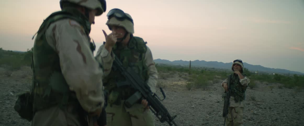 A small group of military soldiers are standing in a field holding their weapons as they speak to each other