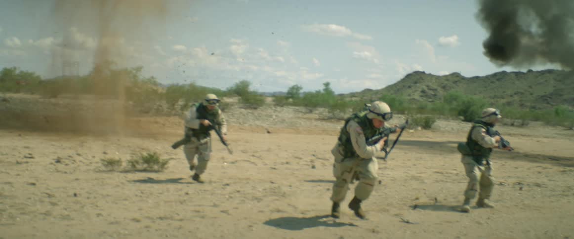 A small group of military soldiers are walking a way from an abandoned automobile in the desert as it explodes and there is an explosion on the ground behind them as they run