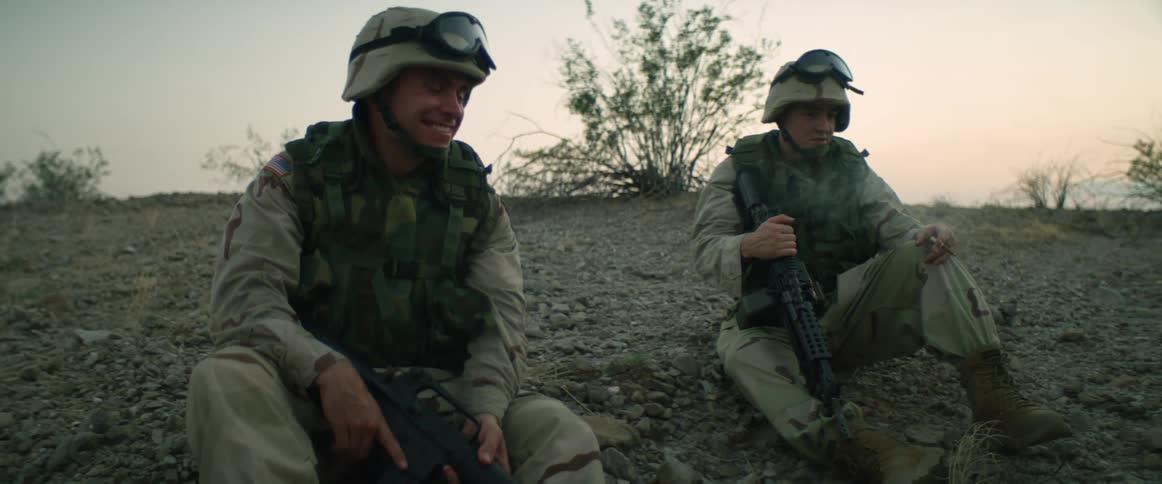 Two military soldiers are sitting along a rocky hillside taking a break and talking to each other