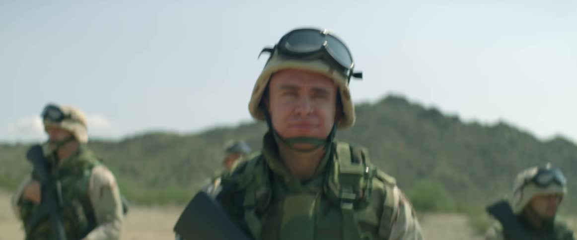 Military patrol walks past wrecked car with hill in the background
