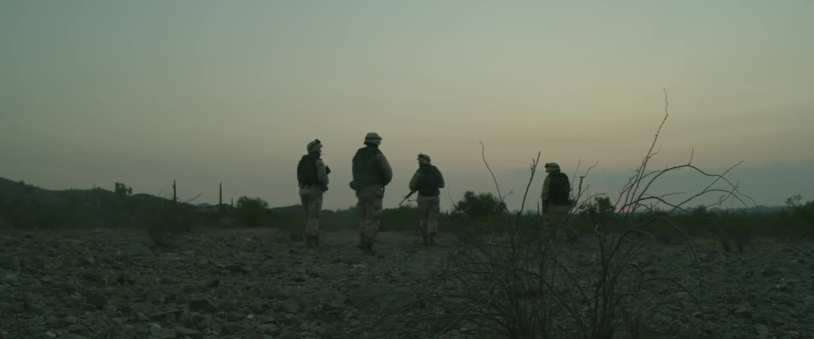 A group of soldiers with military uniforms and weapons patrols the field at dusk