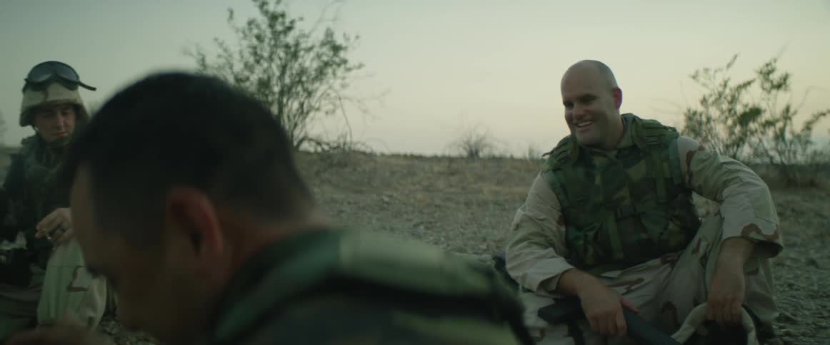 Soldiers are sitting on the sand talking and laughing