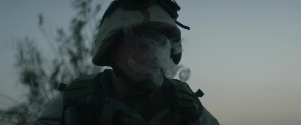 A soldier is standing outside smoking a cigarette