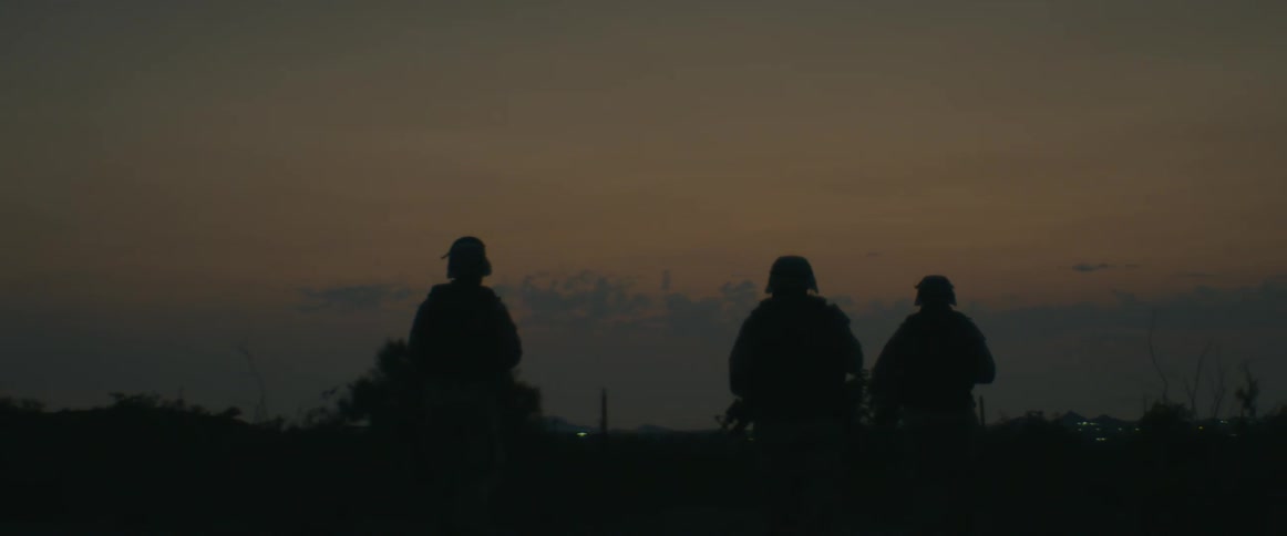 Armed patrol walking through scrub is silhouetted against the red tinted sky