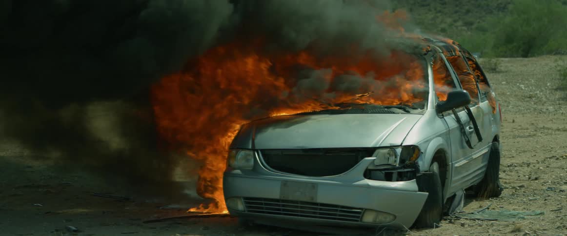 Black smoke billows out of a flaming burning car fire in the desert