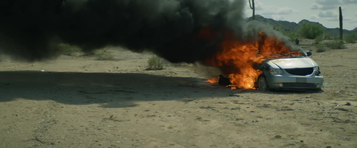 Car parked in a deserted rural area engulfed in flames pouring dark clouds of smoke into the sky