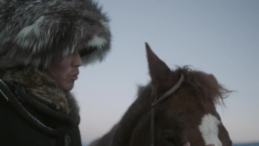 Man wearing fur hat strokes the nose of his horse