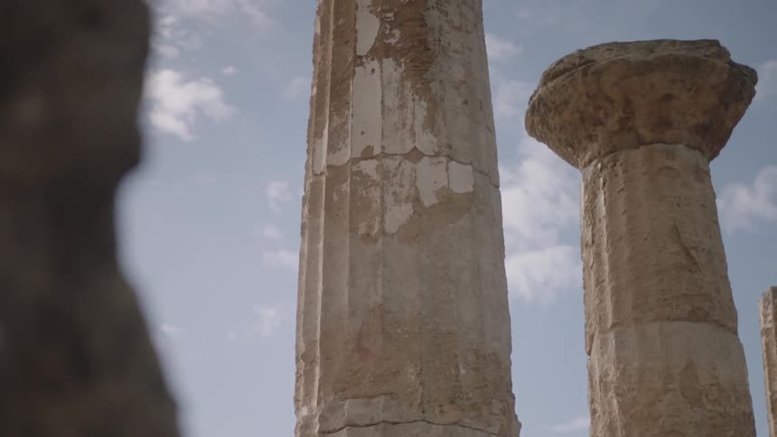 Rocks and ancient columns stand against a partly cloudy sky
