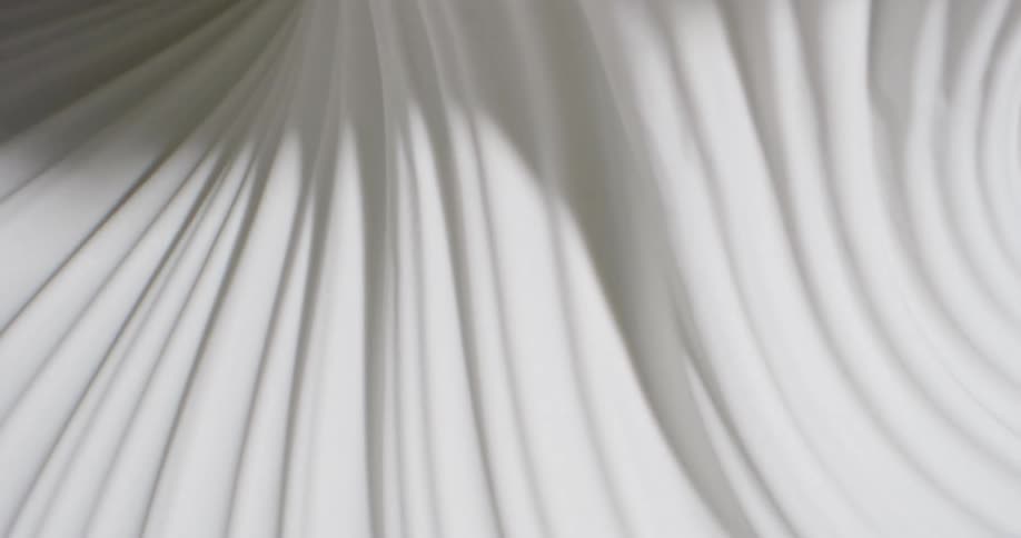 Light shines on a white rippled substance and creates shadows in the grooves as it moves