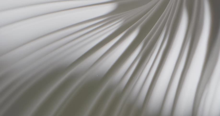 Shadows and light cast over a moving spinning surface of white fabric or porcelain