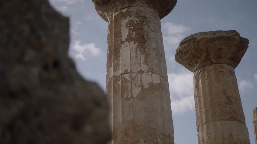 Ancient ruined columns stand against a partially cloudy day sky