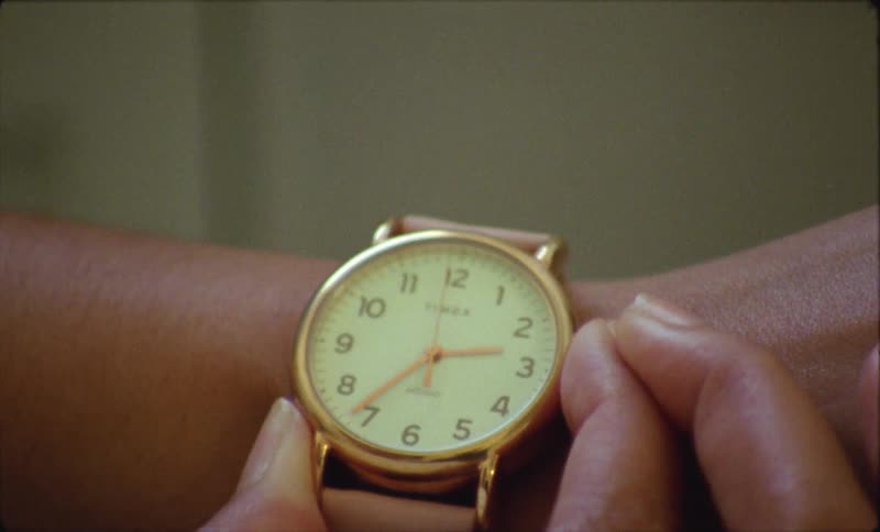 Woman looks at her pink wristwatch