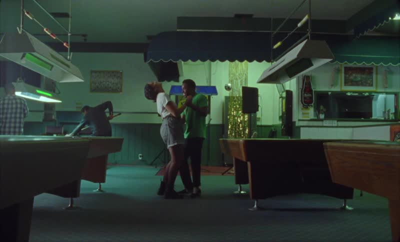 A man and woman smiling and laughing while dancing next to pool tables in a bar