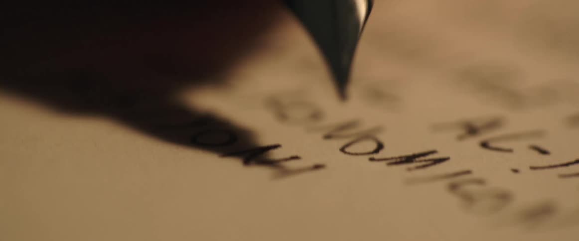 Close up of the tip of a fountain pen writing with black ink on a sheet of white paper