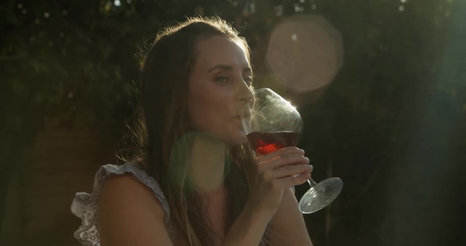 A young white woman is drinking some wine outside in the day time