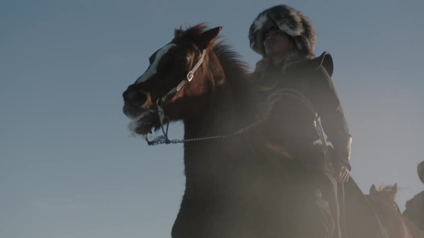 A man wearing a fur hat rides a horse in the daytime