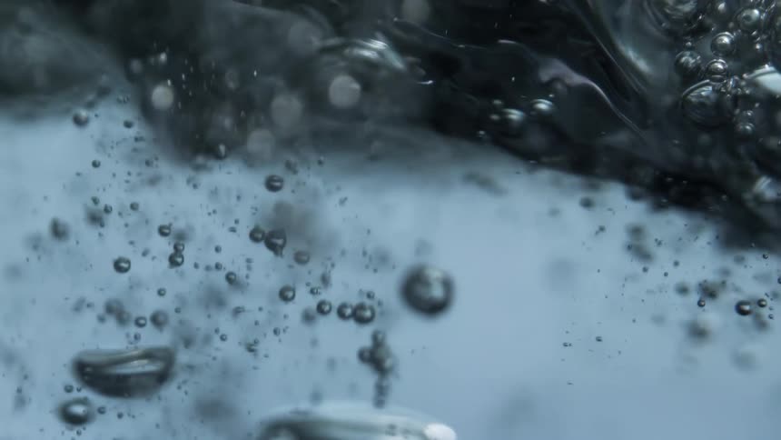 Close up of the ripples and small waves of water flowing over the camera with air bubbles rising