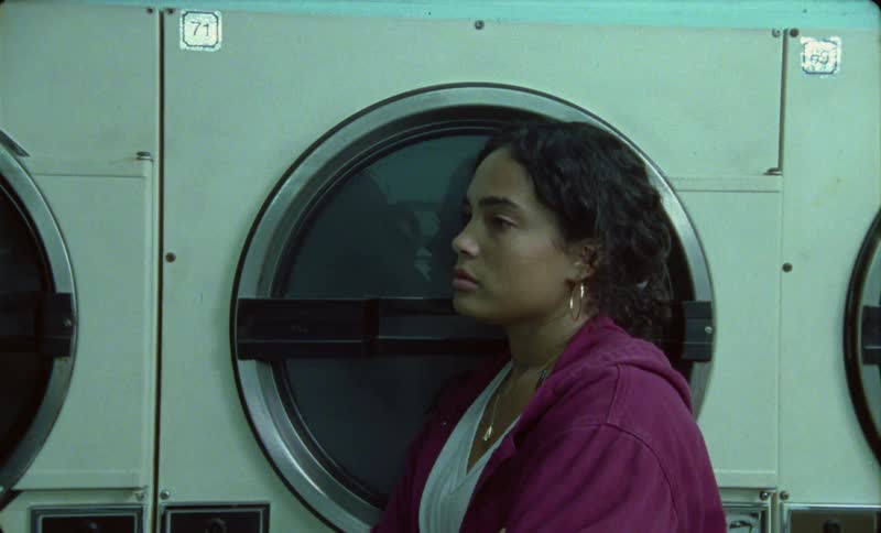 A woman stands in a laundry mat and leans against a dryer