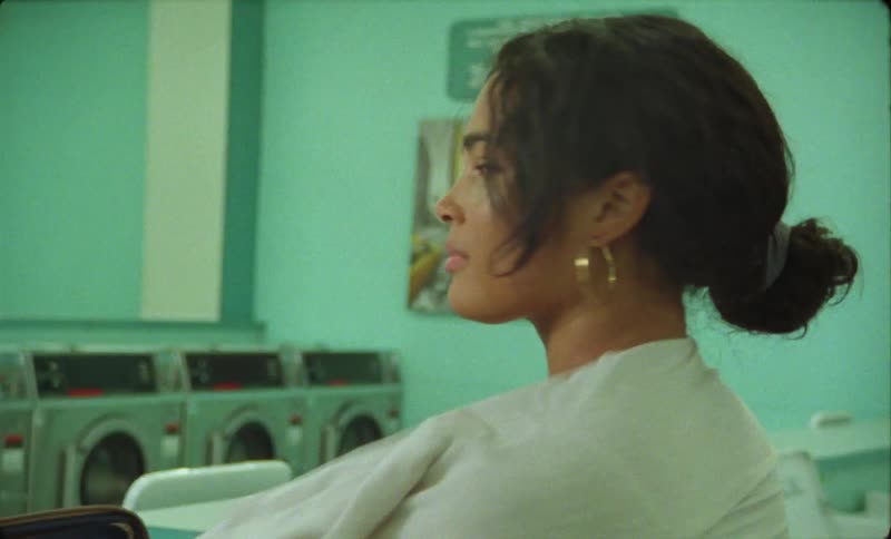 A woman is standing in front of a clothes dryer at a laundry mat and she puts on a shirt