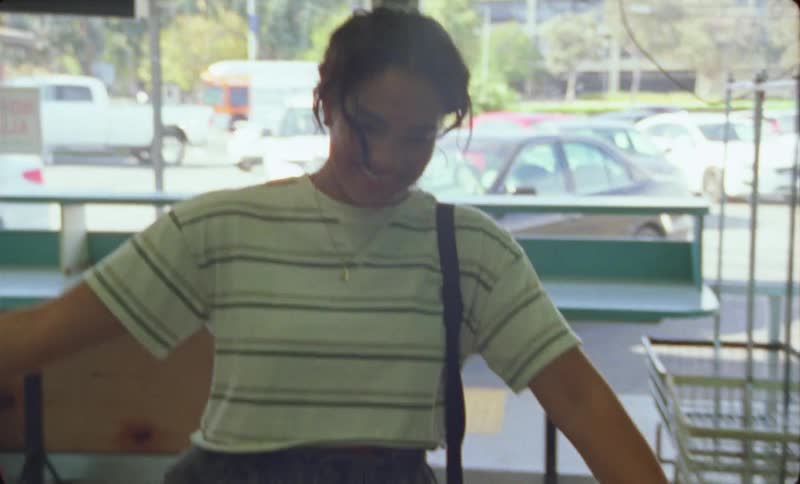A woman walks into a laundry mat and smiles as she walks to a man standing inside and they hug