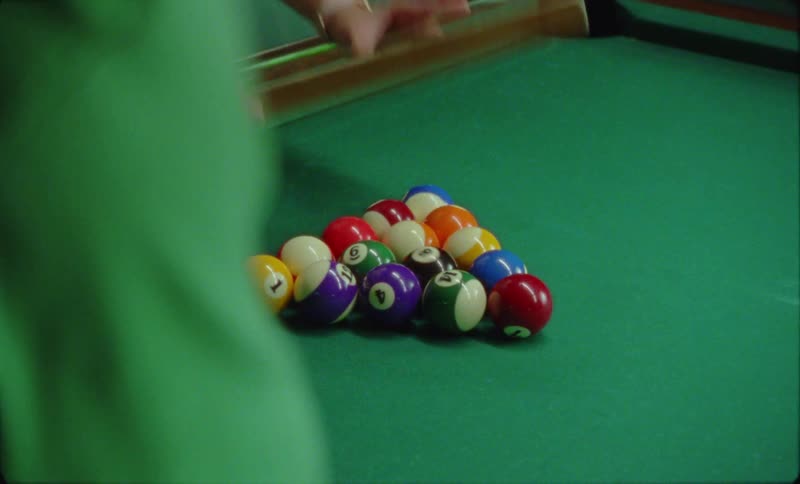 A person uses a pool triangle rack to place billiard balls in their starting position