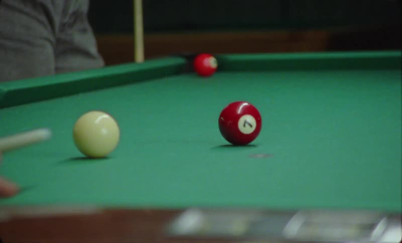 Two people are playing pool and one player slips and misses the cue ball as they try to take a shot
