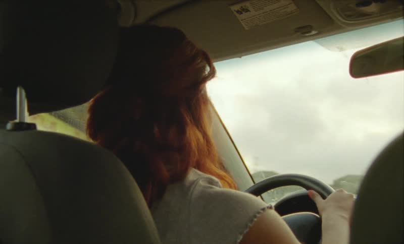Happy woman talks to a passenger while driving a car through town at daytime