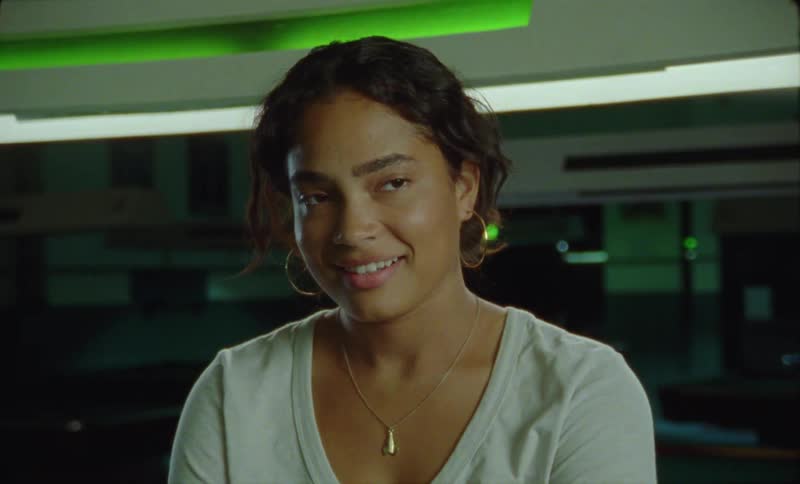 A young woman is standing in a room with lights on the ceiling with a smile on her face
