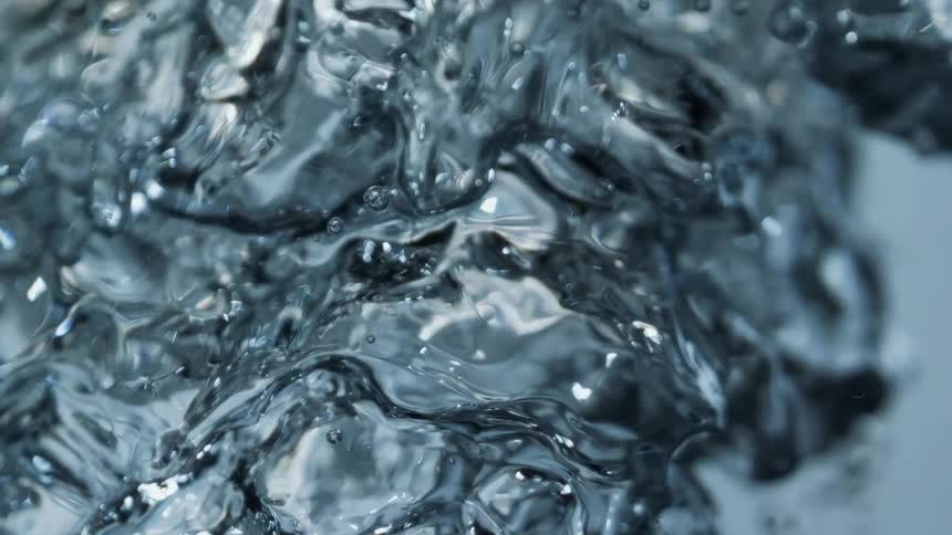 Water splashes up spreading drops into the air and running down side of container