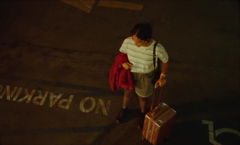 A young hispanic woman is outside at night time holding her luggage