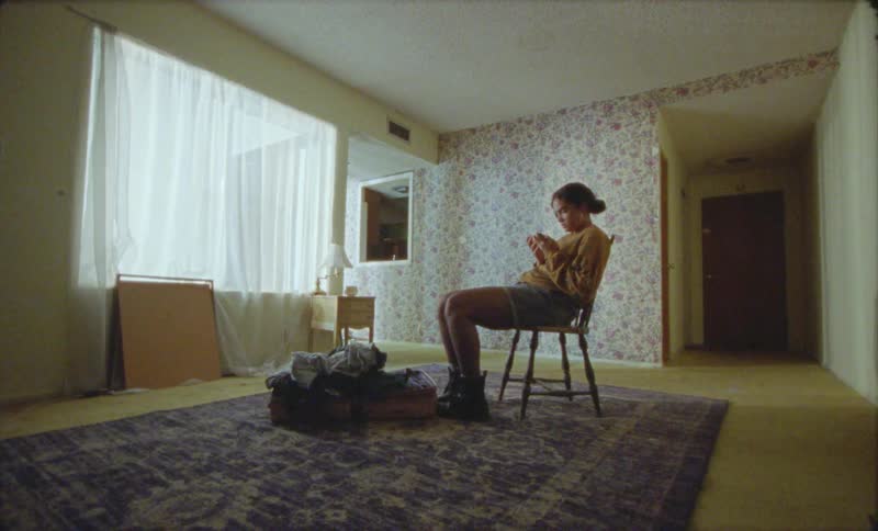 Young woman sitting on a chair next to an open suitcase in the middle of an empty room waiting
