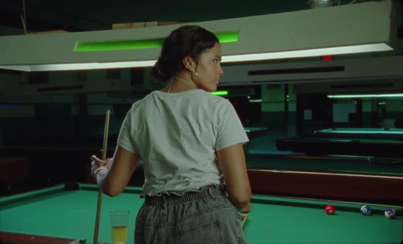 There is a young hispanic woman playing pool at night time