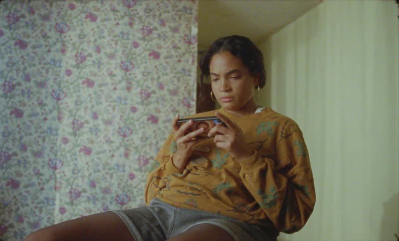 Woman sits in chair in wallpapered room and views video on smartphone